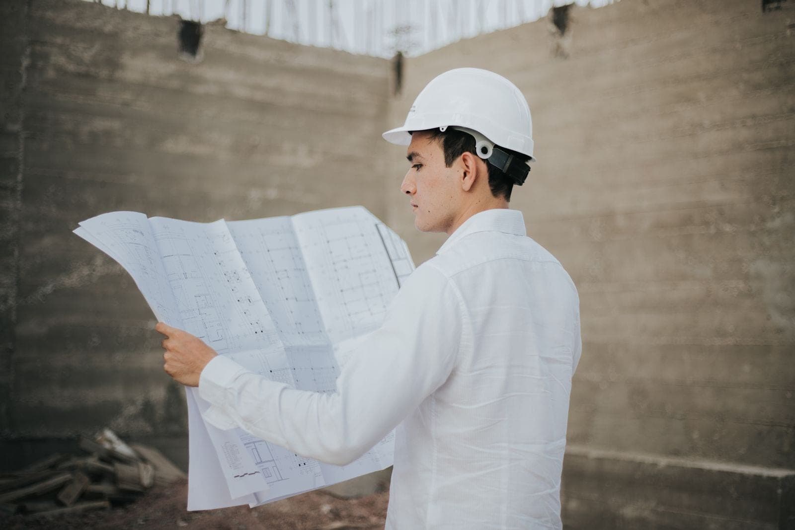 Ingeniero con casco blanco revisa los planos de una obra en construcción